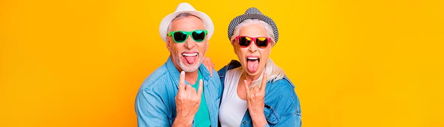 Un homme et une femme d’âge mûr sur un fond jaune vif. Ils portent des chapeaux et de lunette de soleil colorés. Ils tirent la langue de façon provocatrice en souriant et font un signe rock n roll de la main.