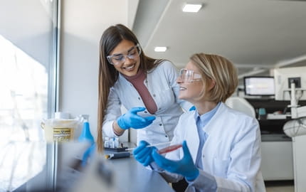 Deux professionnelles de santé échangent au sein d’un laboratoire, elles portent des gants et des lunettes de protection 