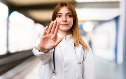 soignante faisant un geste de la main signifiant stop, dans un couloir d’un établissement de santé  