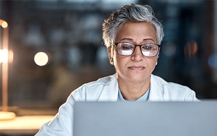 une femme médecin assise à son bureau, concentrée sur son ordinateur portable, en recherche de sa prochaine opportunité professionnelle