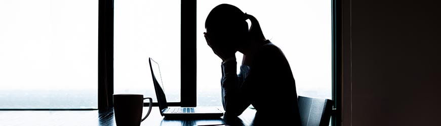 Femme au travail, devant son ordinateur portable se tenant le visage dans les mains en signe de très grande fatigue.