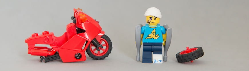 Accident de moto représenté en Lego, avec un moto rouge cassée, roue arrière sur le côté et un personnage Lego, jambe gauche dans le platre, béquille et bandage à la tête.