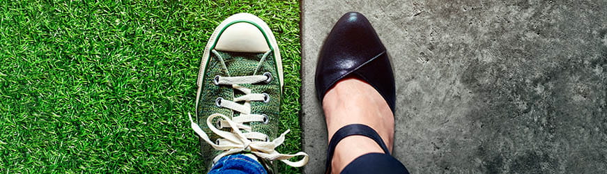 Image coupée en deux. D’un côté un pied chaussé d’une basket poser sur du gazon, de l’autre un pied chaussé d’un escarpin de ville sur de l’asphalte. 