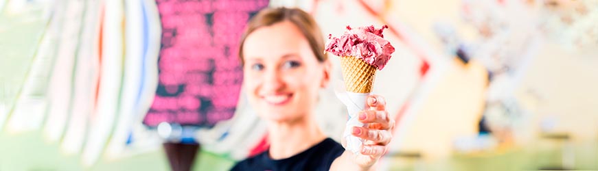 Jeune femme souriante, tendant à quelqu’un, une grosse glace à la fraise en cornet.