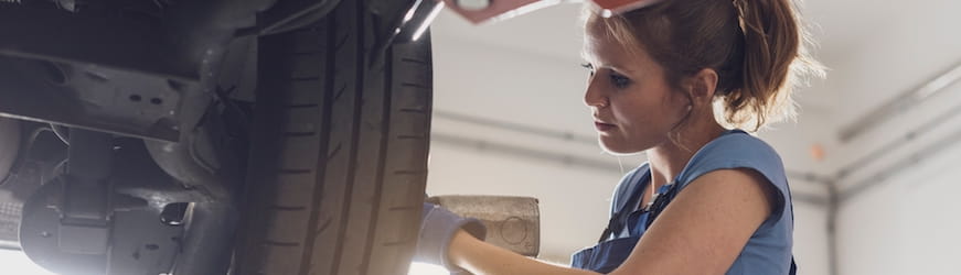 Une jeune mécanicienne en train de monter une roue de voiture