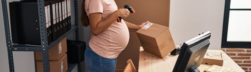 Une jeune femme enceinte, souriante, qui travaille dans un bureau : elle est en train de scanner un colis