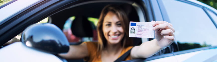 Une jeune salariée dans une voiture, qui montre le permis de conduire qu’elle vient d’obtenir