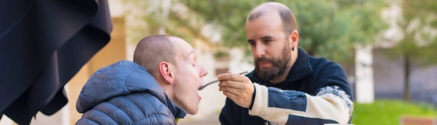 Un homme à la terrasse d’un restaurant, qui aide son frère en situation de handicap à manger.