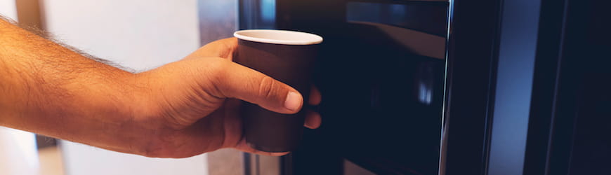 La main d’un salarié attrapant un gobelet d’une machine à café. 
