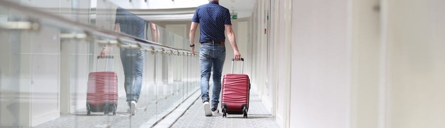 Un salarié en grand déplacement professionnel, tirant sa valise dans un couloir d’hôtel.