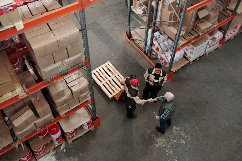 Deux personnes dans un entrepôt se serrent la main avant de ranger des palettes