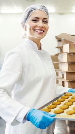 Jeune femme souriante portant une charlotte, des gants et une combinaison de protection dans un entrepôt de produits agroalimentaires.