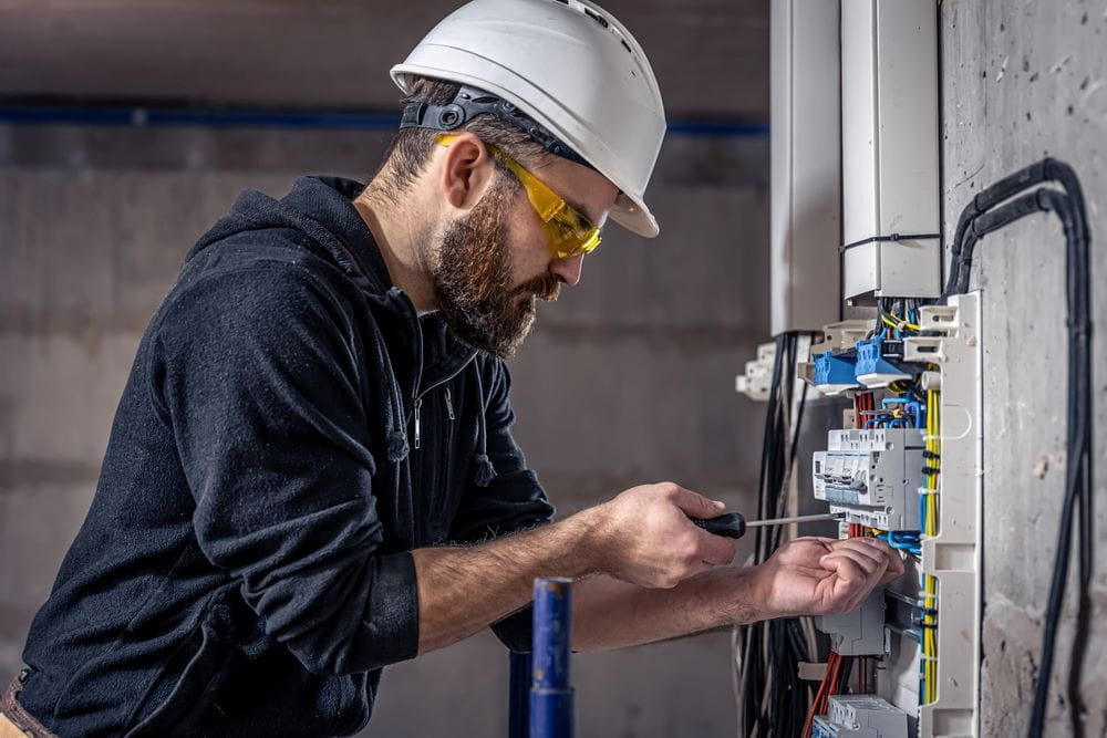Un électricien de sexe masculin travaille dans un tableau de contact avec un câble électrique.