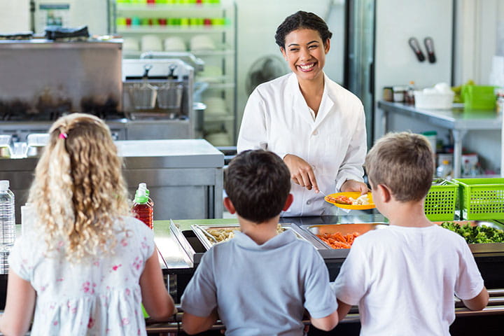 cheerful-woman-serving-food-to-schoolchildren-in-canteen