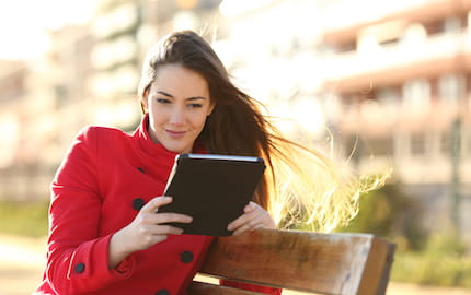 Une femme assisse sur un banc recherche un nouveau profil pour son entreprise depuis sa tablette sur les réseaux sociaux