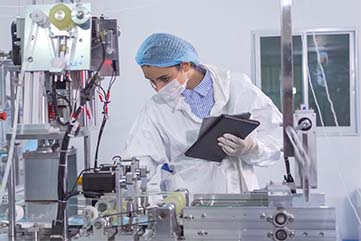 femme technicienne chimiste, penchée sur une préparation chimique dans un atelier, elle porte une blouse, une charlotte et des gants de protection